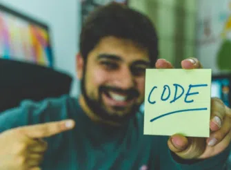 Uomo sorridente mostra un post-it con la parola “CODE”, simbolo della mentalità tecnica di molti founder.