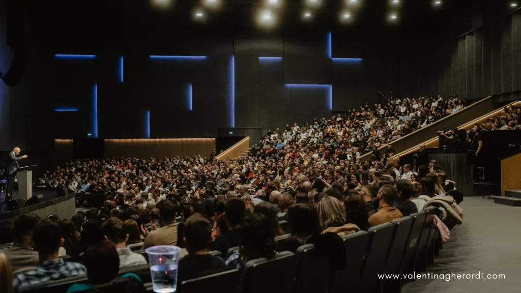 Relatore sul palco davanti a un grande pubblico durante un convegno professionale in auditorium