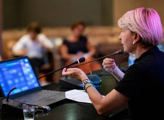 Professionista durante un intervento pubblico al microfono, in un contesto di incontro e confronto professionale.